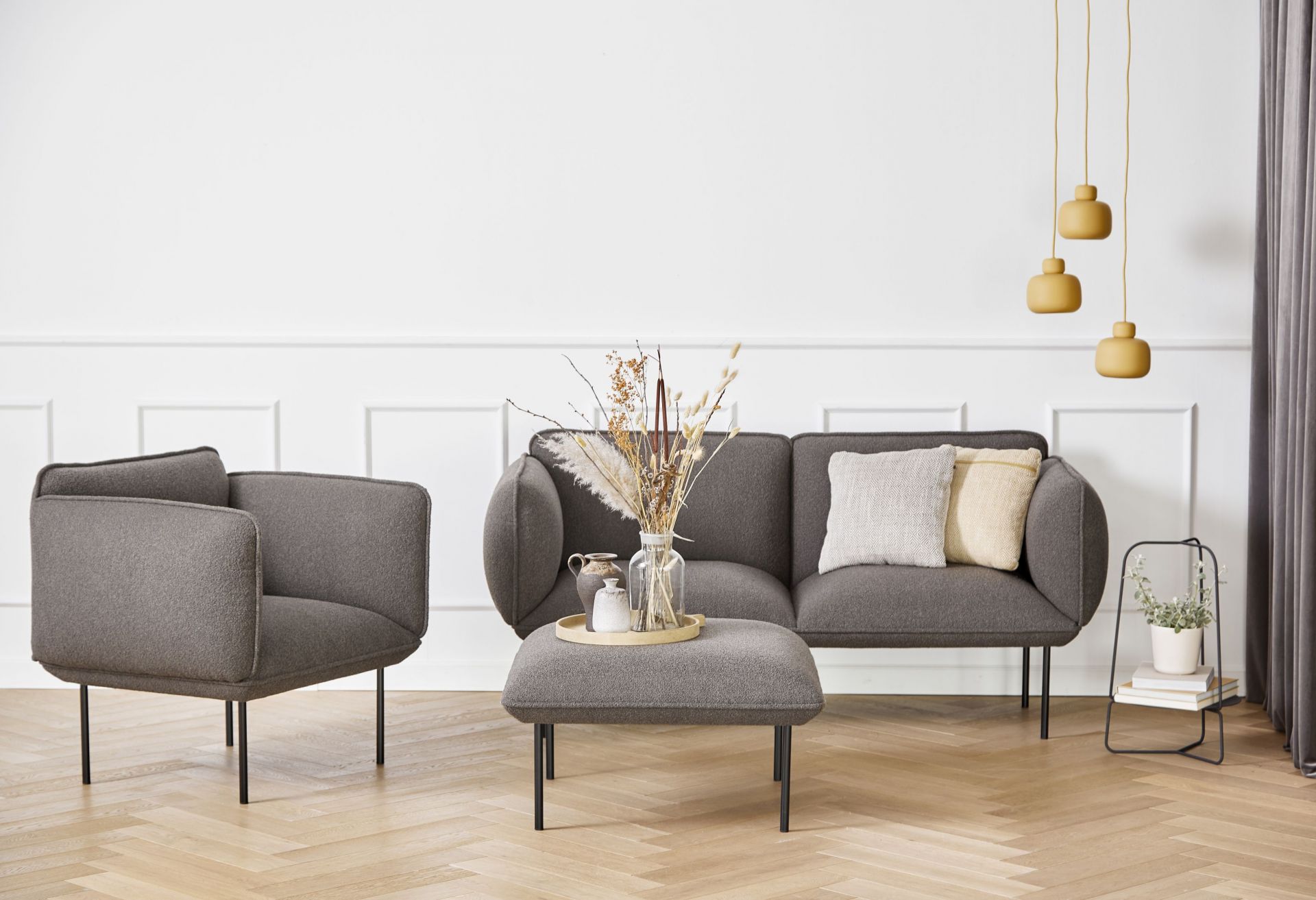 Wohnzimmer-Szene mit grauer Couch, Sessel, Hocker und drei gelben Stone Pendant Pendelleuchten von Woud über dem Sofa.