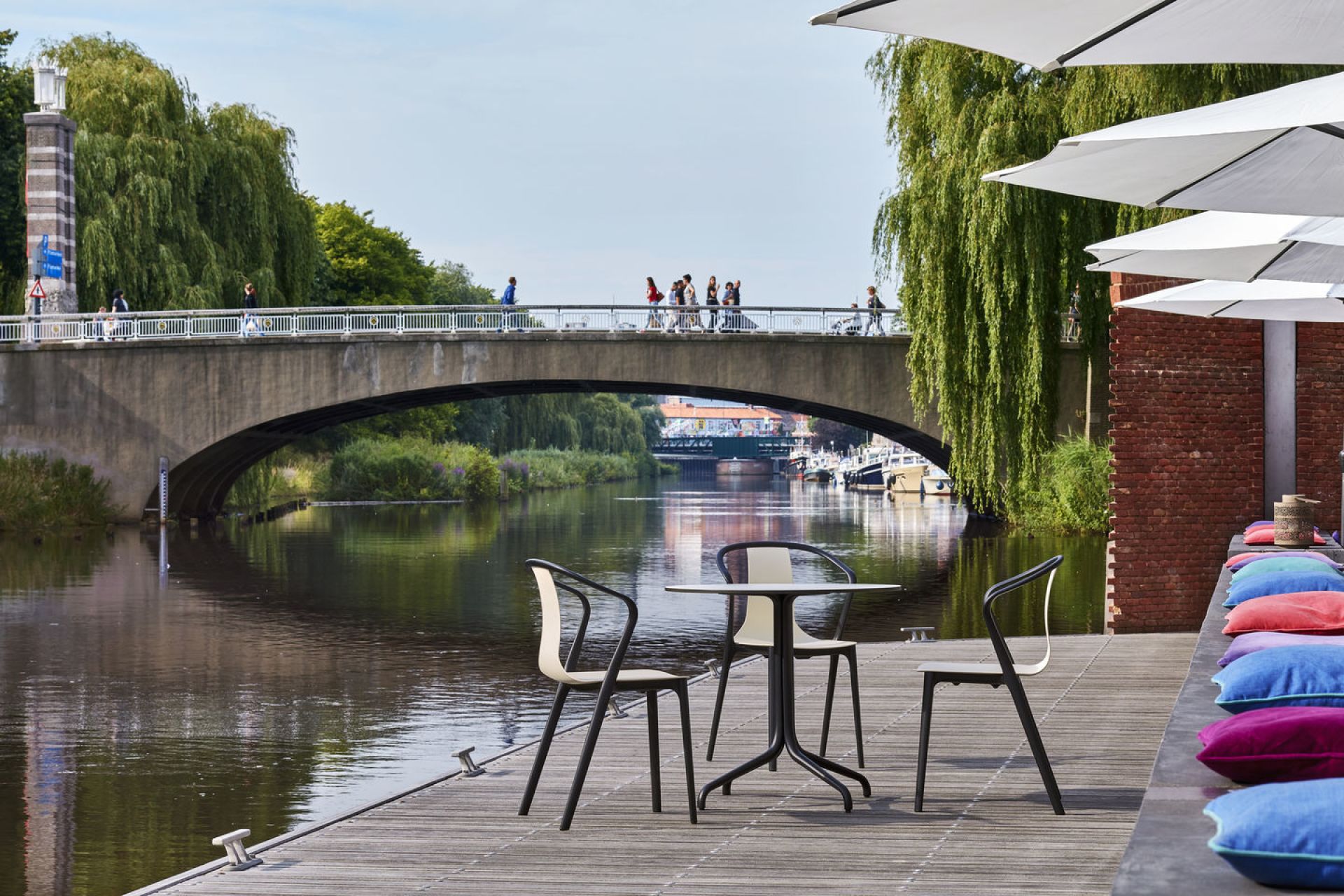 Vitra Belleville Armchair Plastic Stühle und Tisch auf Holzterrasse am Fluss mit Brücke im Hintergrund.