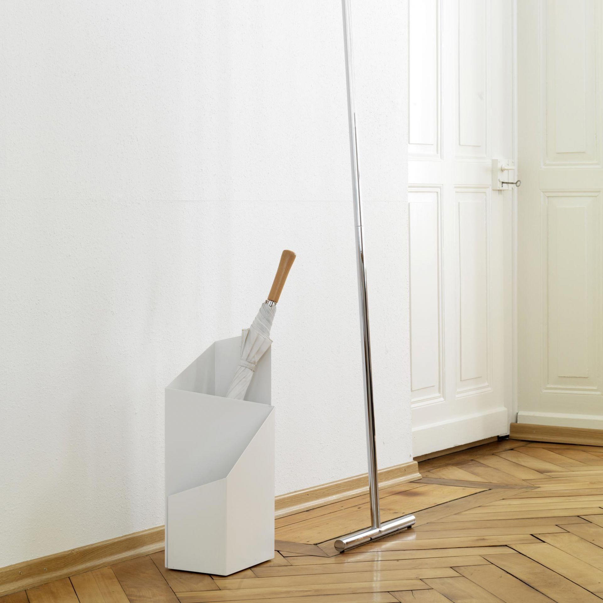 Weißer Via Schirmständer von Mox mit Regenschirm und Garderobenständer im minimalistischen Flur auf Parkettboden.