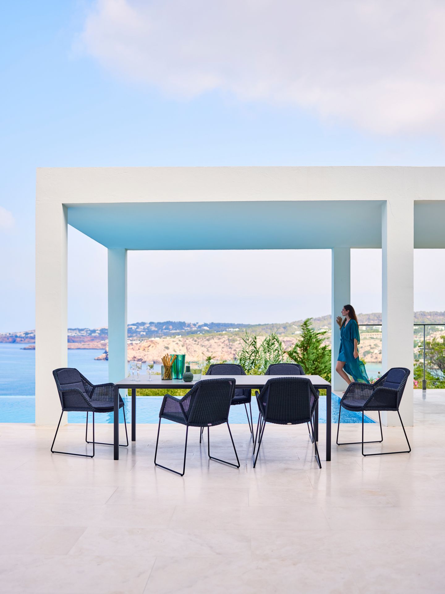 Cane-Line Esstisch Pure Outdoor mit schwarzen Stühlen auf einer Terrasse mit Meerblick.