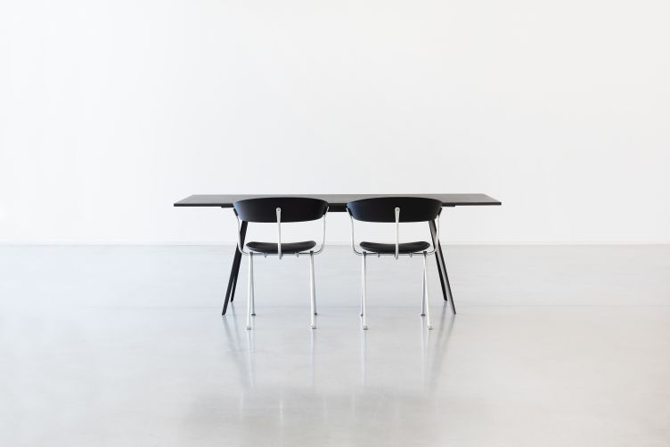 Zwei schwarze Officina Stühle von Magis an einem schwarzen Tisch in minimalistischem Studio.