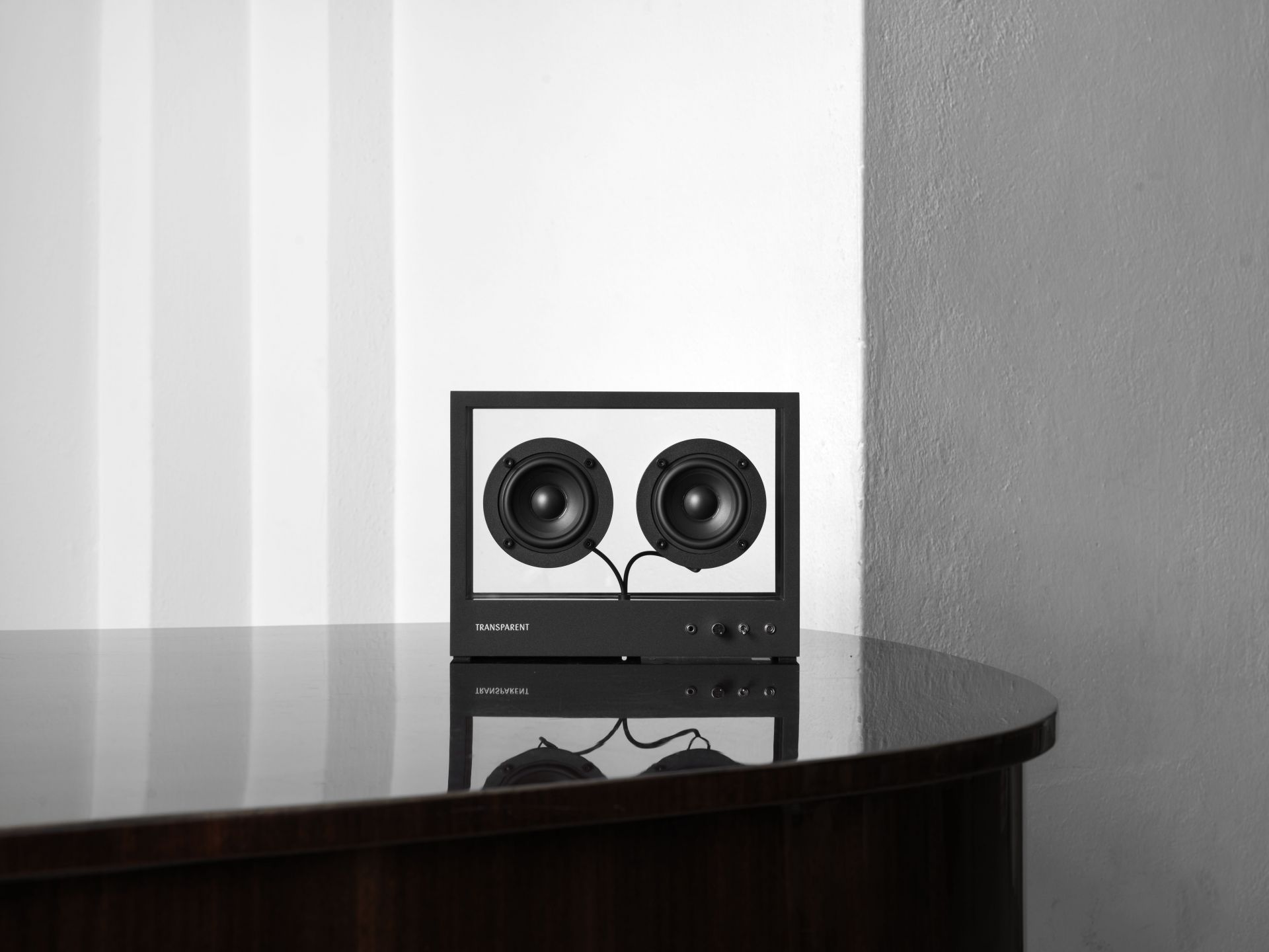 Kleiner transparenter Lautsprecher auf dunklem Tisch, minimalistisches Design, hochwertige Audio-Technik für Musikliebhaber.