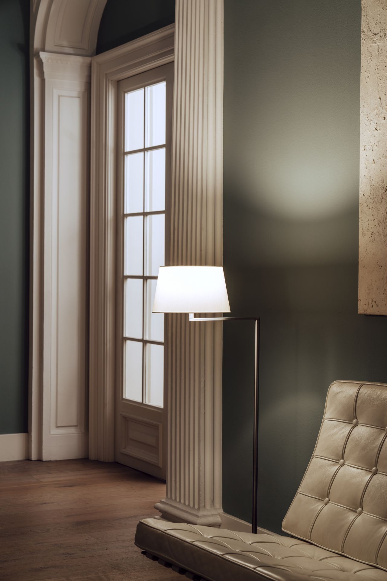 Elegante Santa & Cole Stehleuchte mit weißem Schirm neben einem Ledersofa in stilvollem Interieur.