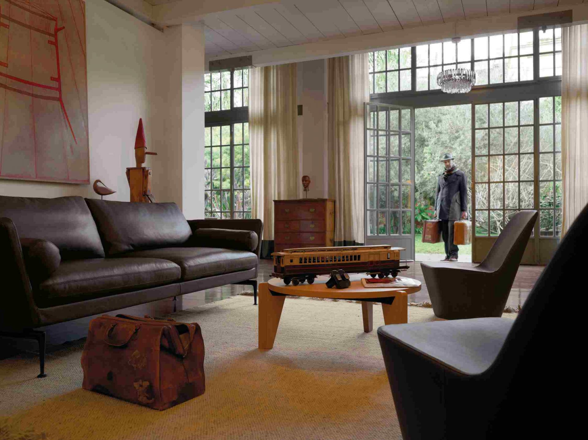 Wohnzimmer mit braunem Suita Sofa von Vitra, Sessel und Mann mit Koffern im Hintergrund.