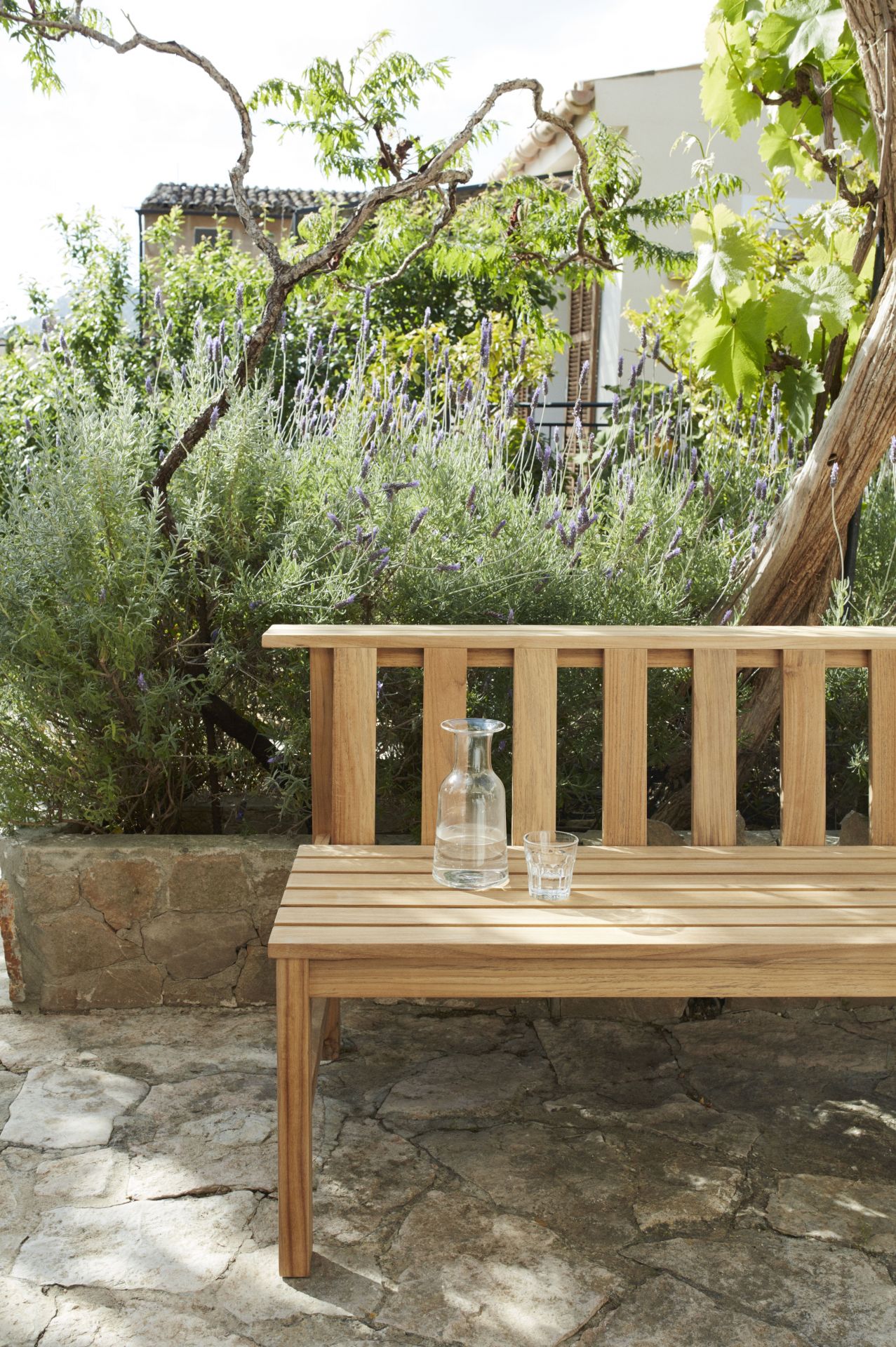 Cadence Bank Teakholz Gartenbank von Skagerak by Fritz Hansen mit Wasserflasche und Glas.