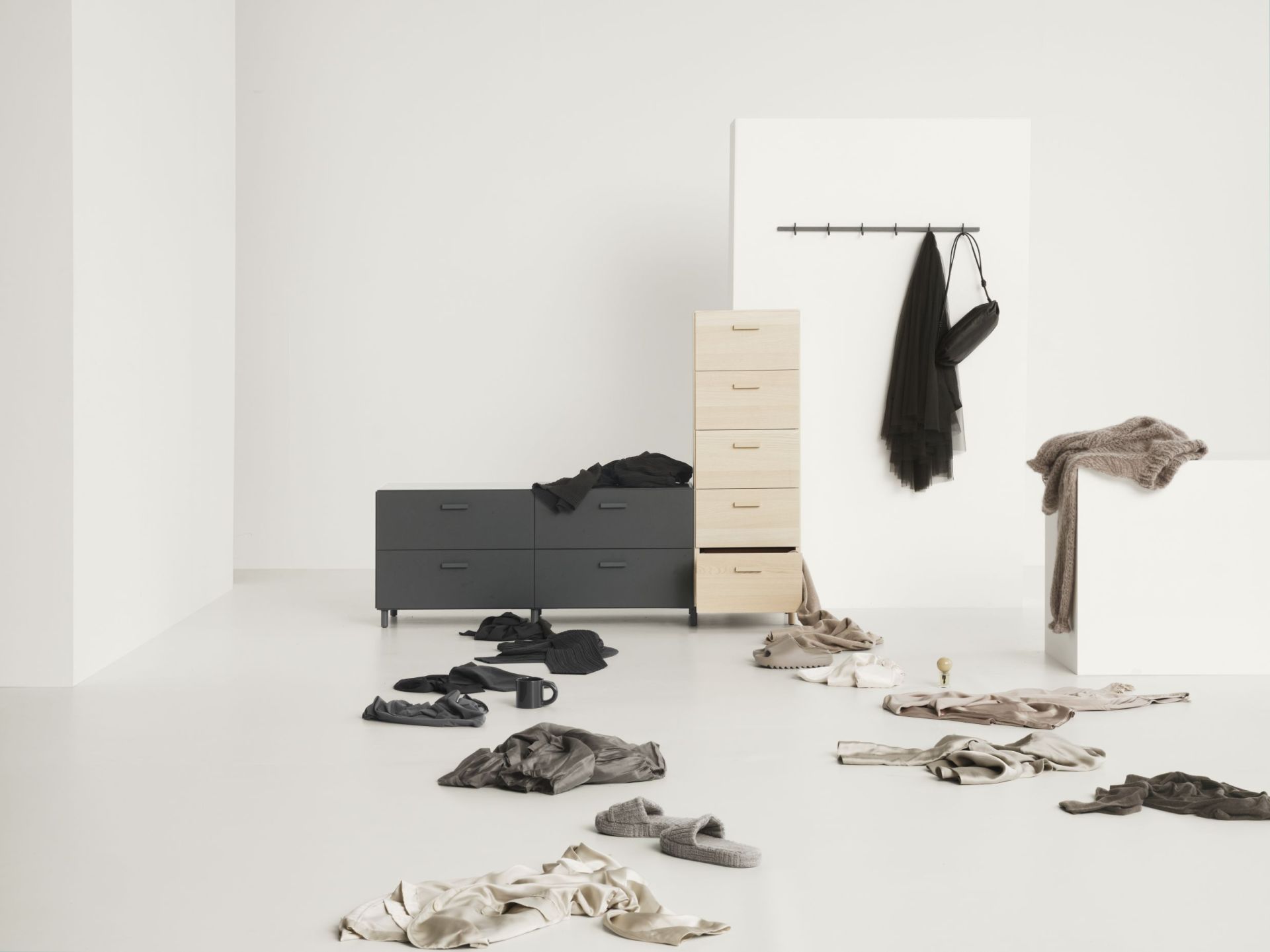 Graue Relief Hakenleiste von String Furniture an weißer Wand mit Kleidung und Accessoires.