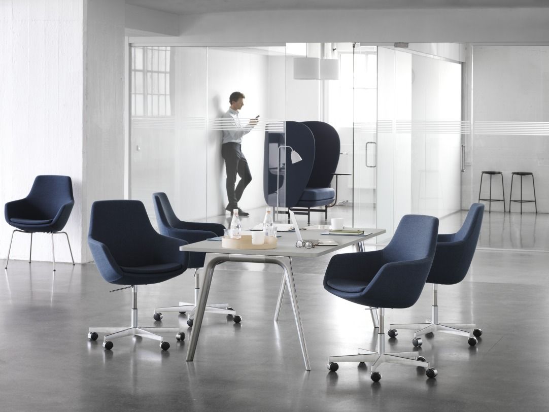 Innenraum mit Fritz Hansen Büromöbeln: Blaue Drehstühle mit Armlehne und Caravaggio Pendelleuchten über einem Konferenztisch.