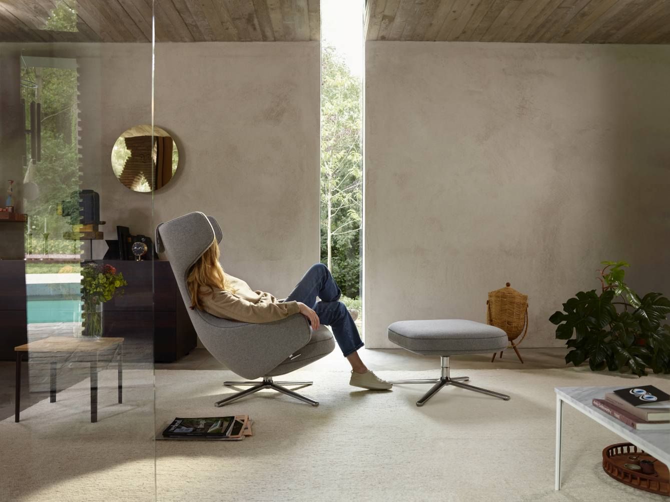 Frau entspannt im grauen Grand Repos Sessel mit Ottoman von Vitra in modernem Wohnzimmer.