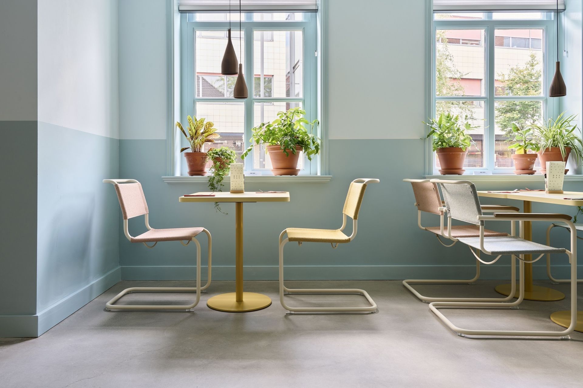 Innenaufnahme mit Thonet S 34 Freischwinger Stühlen in verschiedenen Farben an gelben Tischen vor hellblauen Wänden.