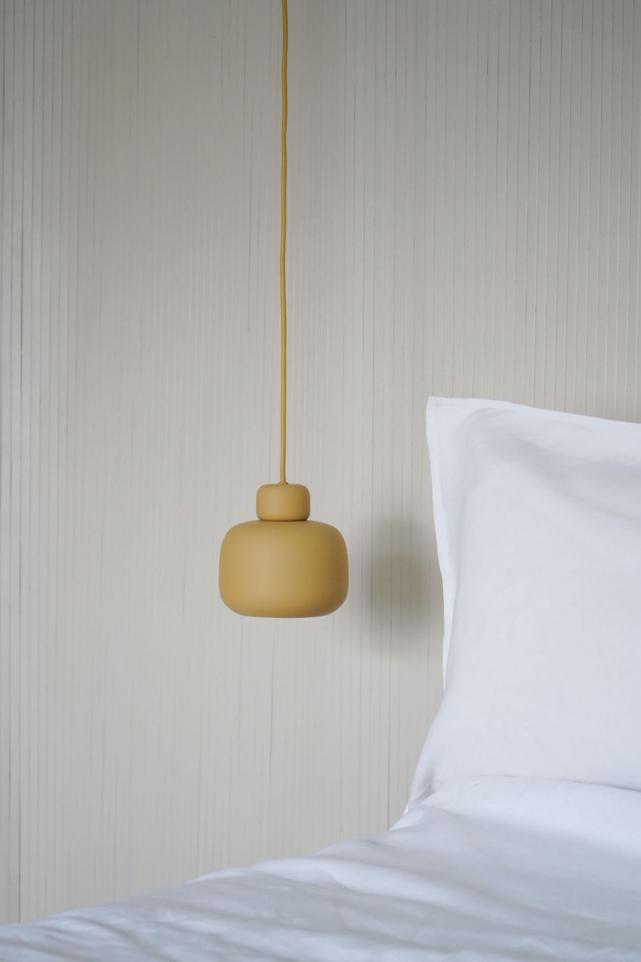 Nahaufnahme der kleinen Stone Pendant Pendelleuchte von Woud in Gelb über einem Bett.