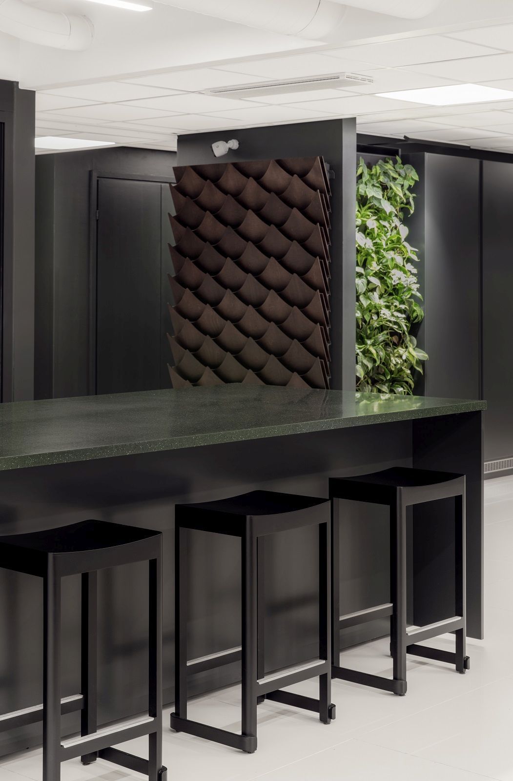 Drei schwarze Atelier Barhocker von Artek an einer Küchentheke in modernem Interieur.