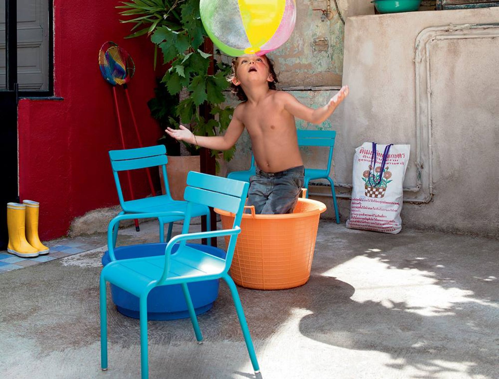 Luxembourg Kinderstuhl von Fermob im Garten: Junge spielt mit Ball, umgeben von blauen Outdoor-Stühlen.