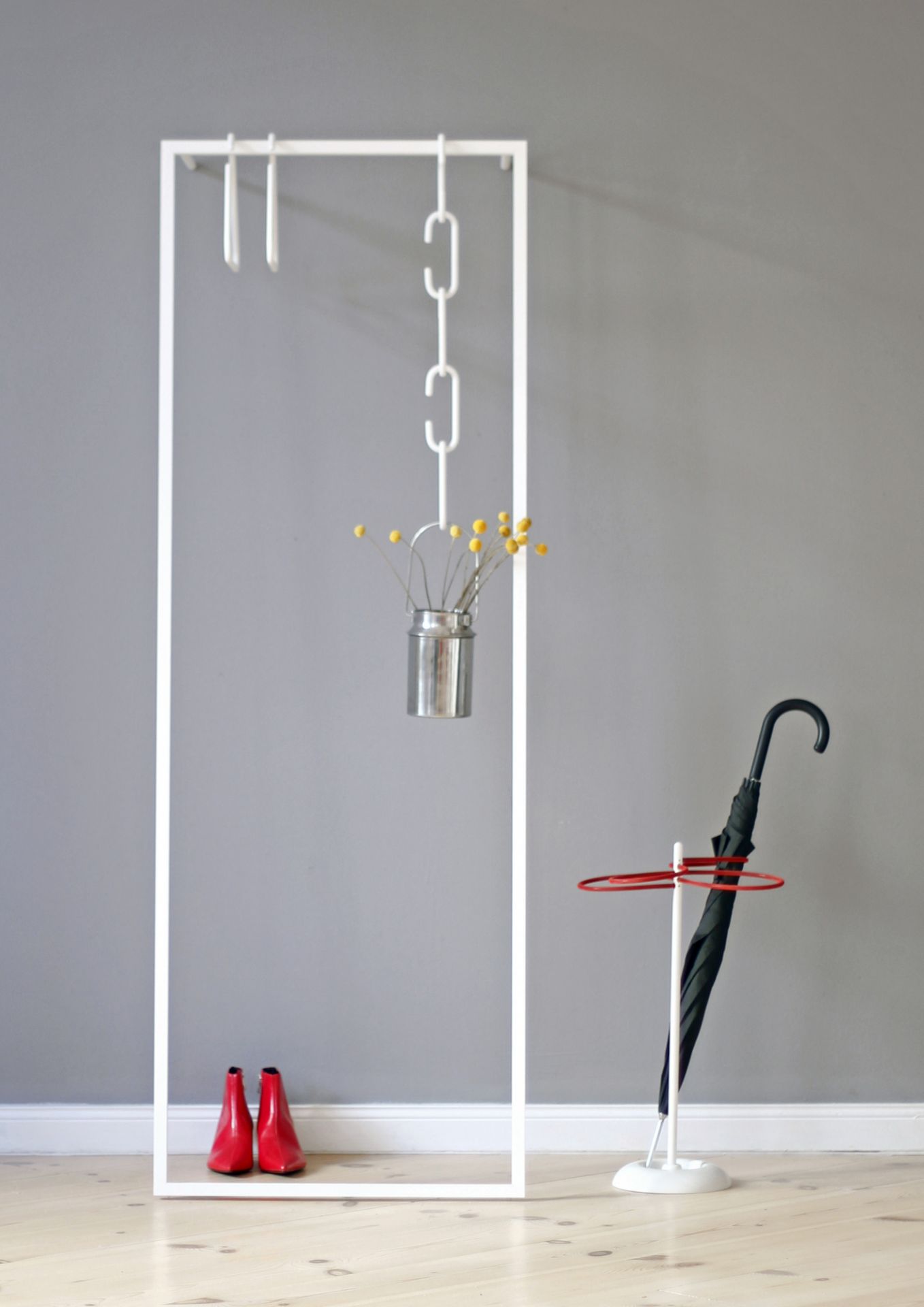 Weiße Leano Anlehngarderobe von Roomsafari mit roten Schuhen, Regenschirm und Dekoration vor grauer Wand.
