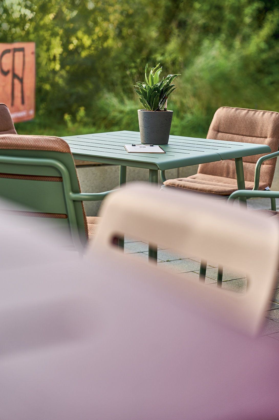 Weishäupl Vapio Tisch Outdoor: Grüner Gartentisch mit Pflanze und Stühlen im Außenbereich für Terrasse oder Garten.