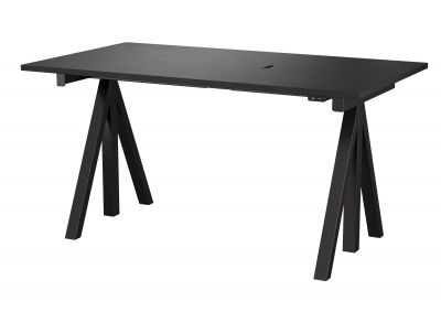Schwarzer Works Schreibtisch höhenverstellbar von String Furniture mit trapezförmigen Beinen und Kabeldurchlass für ergonomisches Arbeiten.