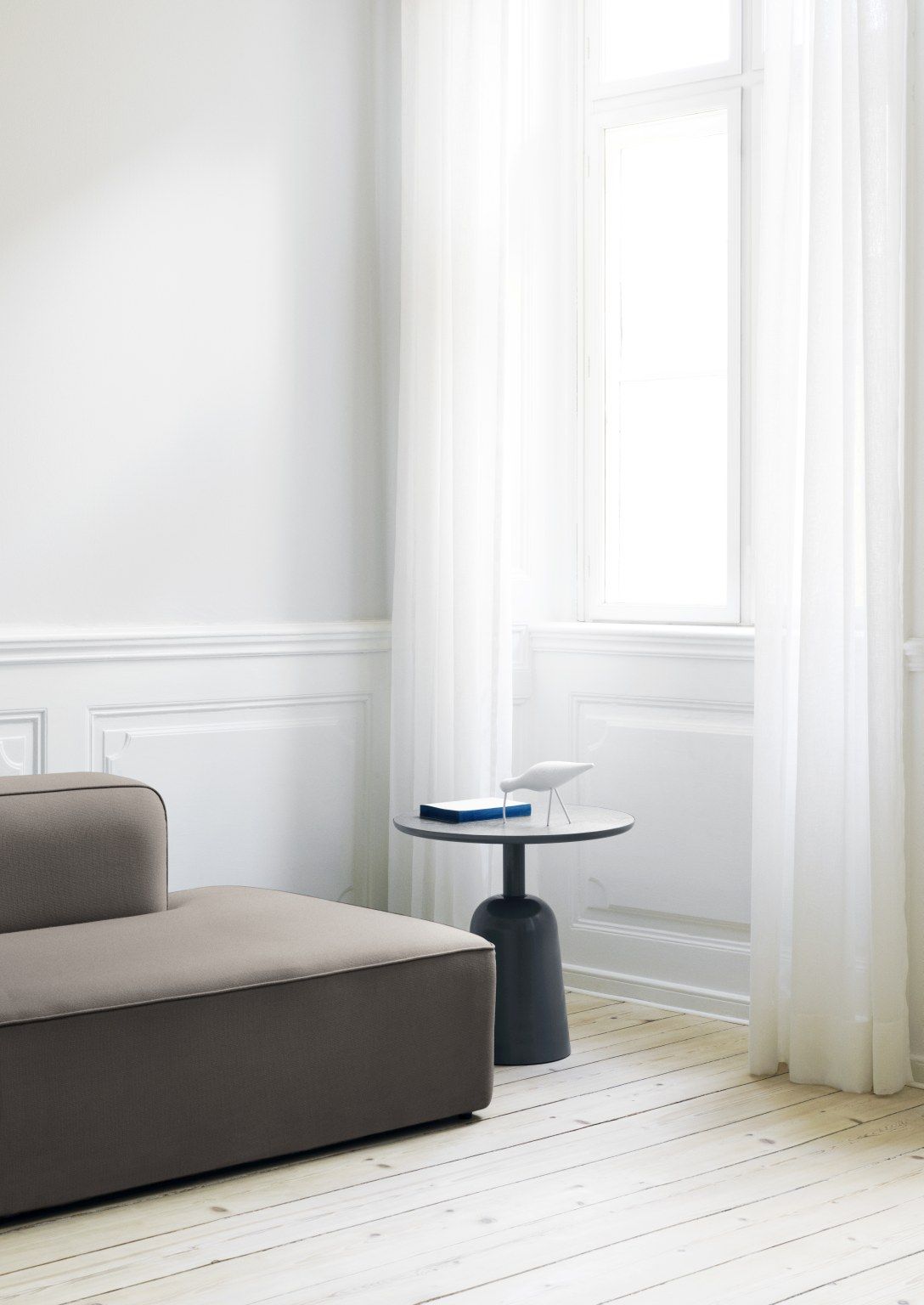 Normann Copenhagen Turn Table Tisch in dunklem Grau neben einem beigen Sofa in hellem Raum.