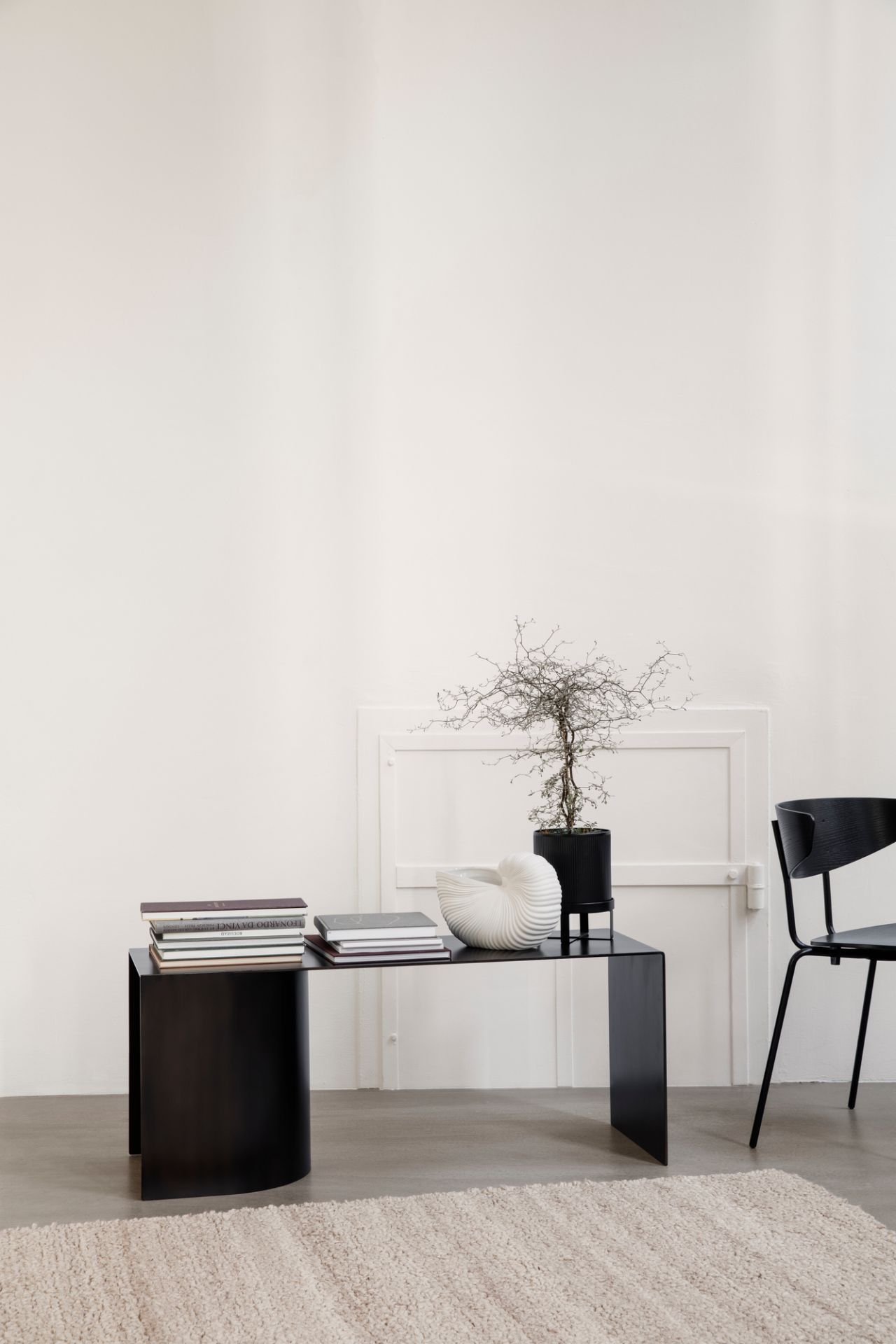 Weiße Ferm Living Shell Pot Vase auf schwarzem Tisch, neben Büchern und Zimmerpflanze.