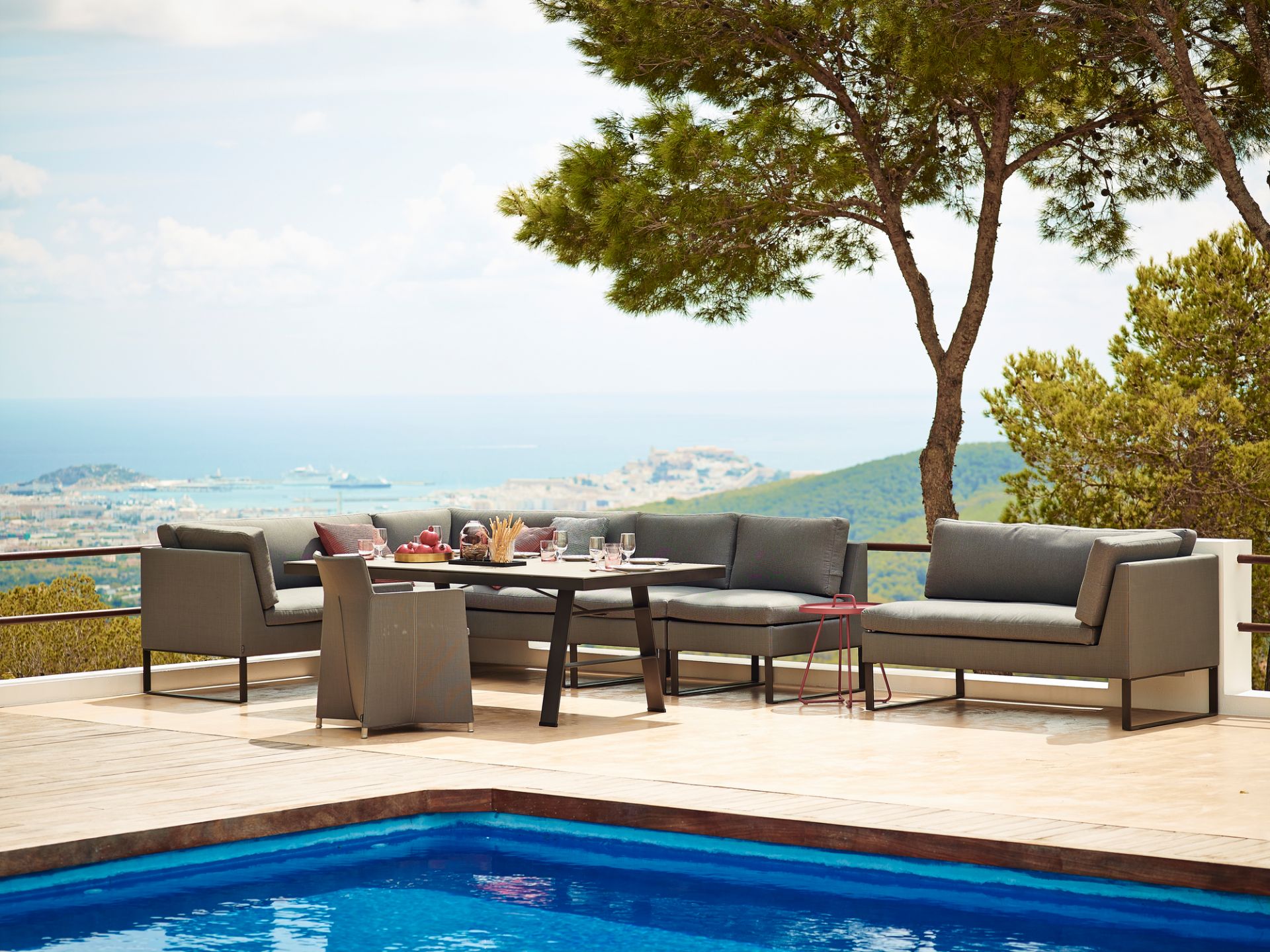 Cane-Line Flex Outdoor Sofa 2-Sitzer links, graues Lounge-Set am Pool mit Meerblick.