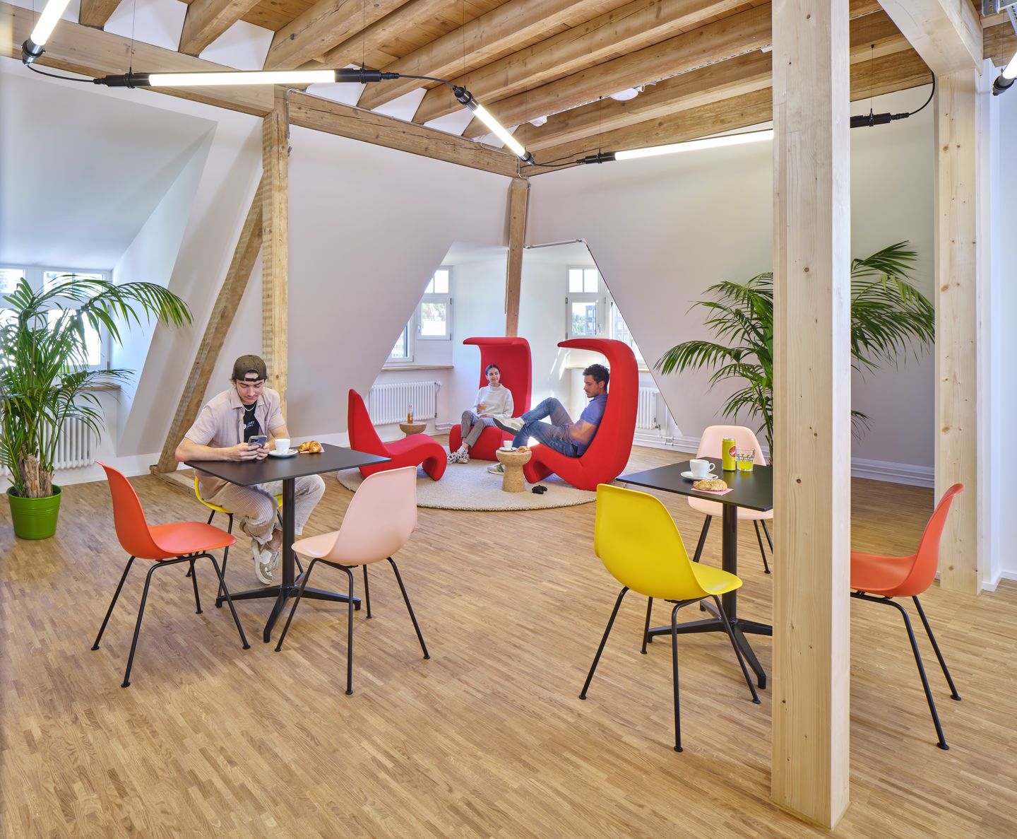 Helles Büro mit Eames Plastic Side Chairs von Vitra in Gelb, Orange und Rosa an schwarzen Tischen.