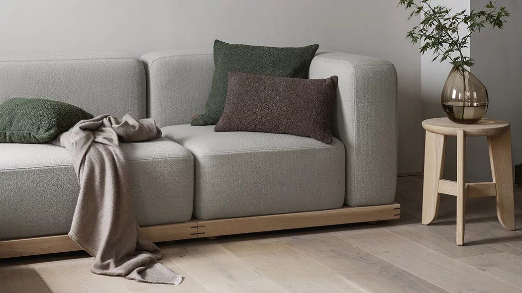 Eli Stool Sitzhocker von Blomus aus Holz neben Sofa mit Kissen und Dekoration.