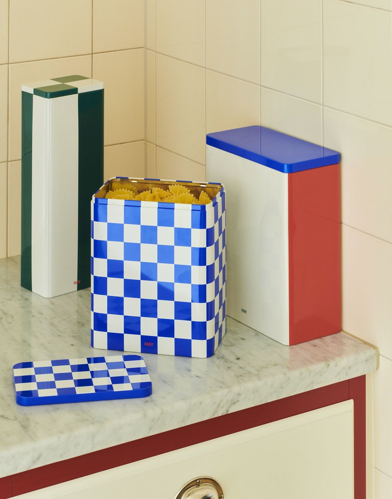 Hay Vorratsdosen-Set: Blaue Aufbewahrungsbox mit Schachmuster, gefüllt mit Pasta, und weitere farbige Dosen.