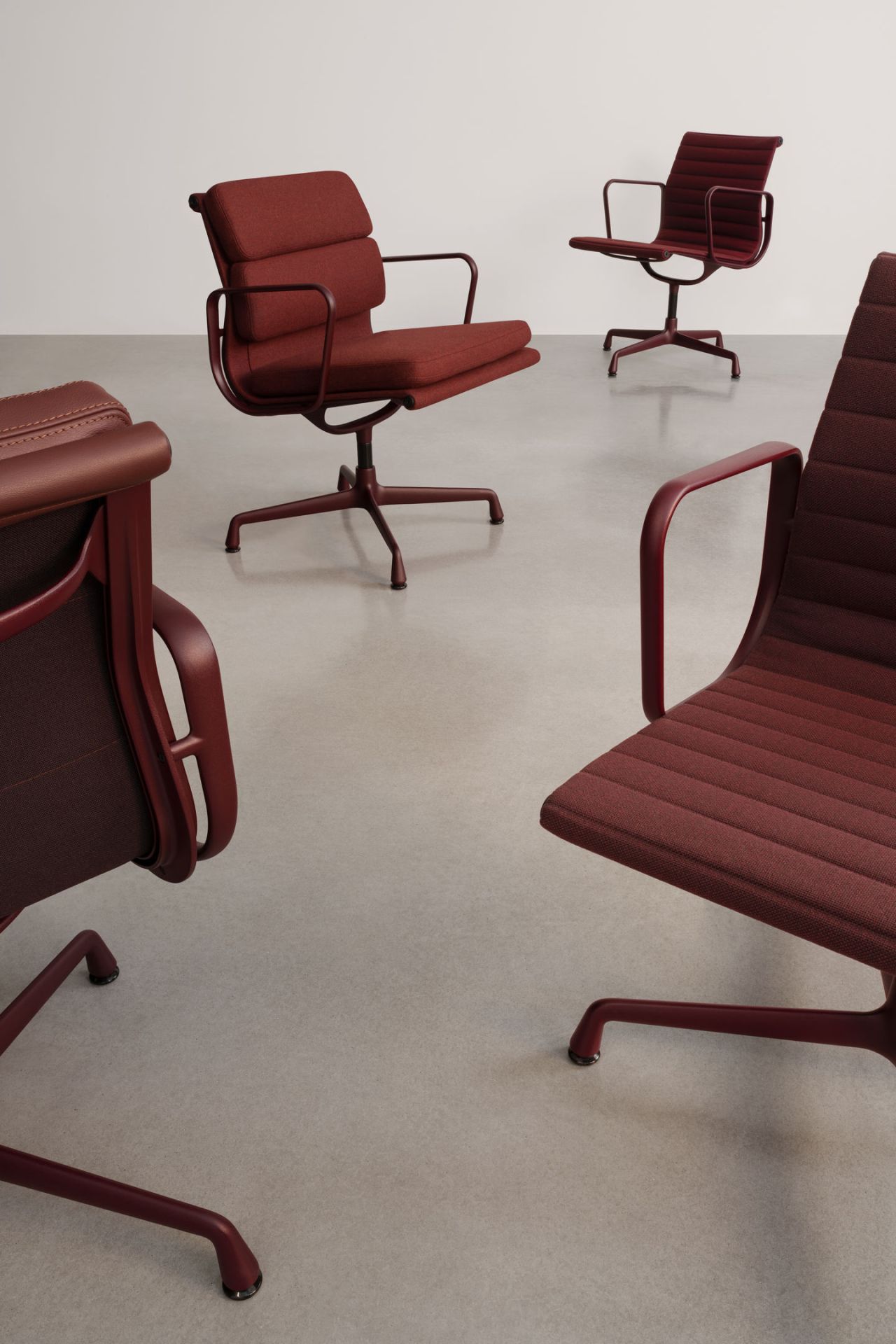 Nahaufnahme von drei roten Vitra Soft Pad Chair EA207 Bürostühlen mit Armlehnen auf grauem Untergrund.