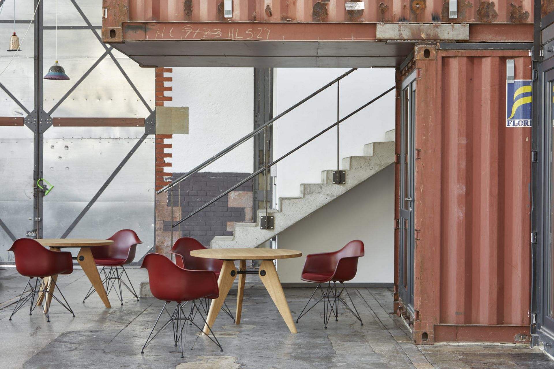 Rote Eames Plastic Arm Chairs DAR von Vitra um Holztische in industriellem Ambiente.