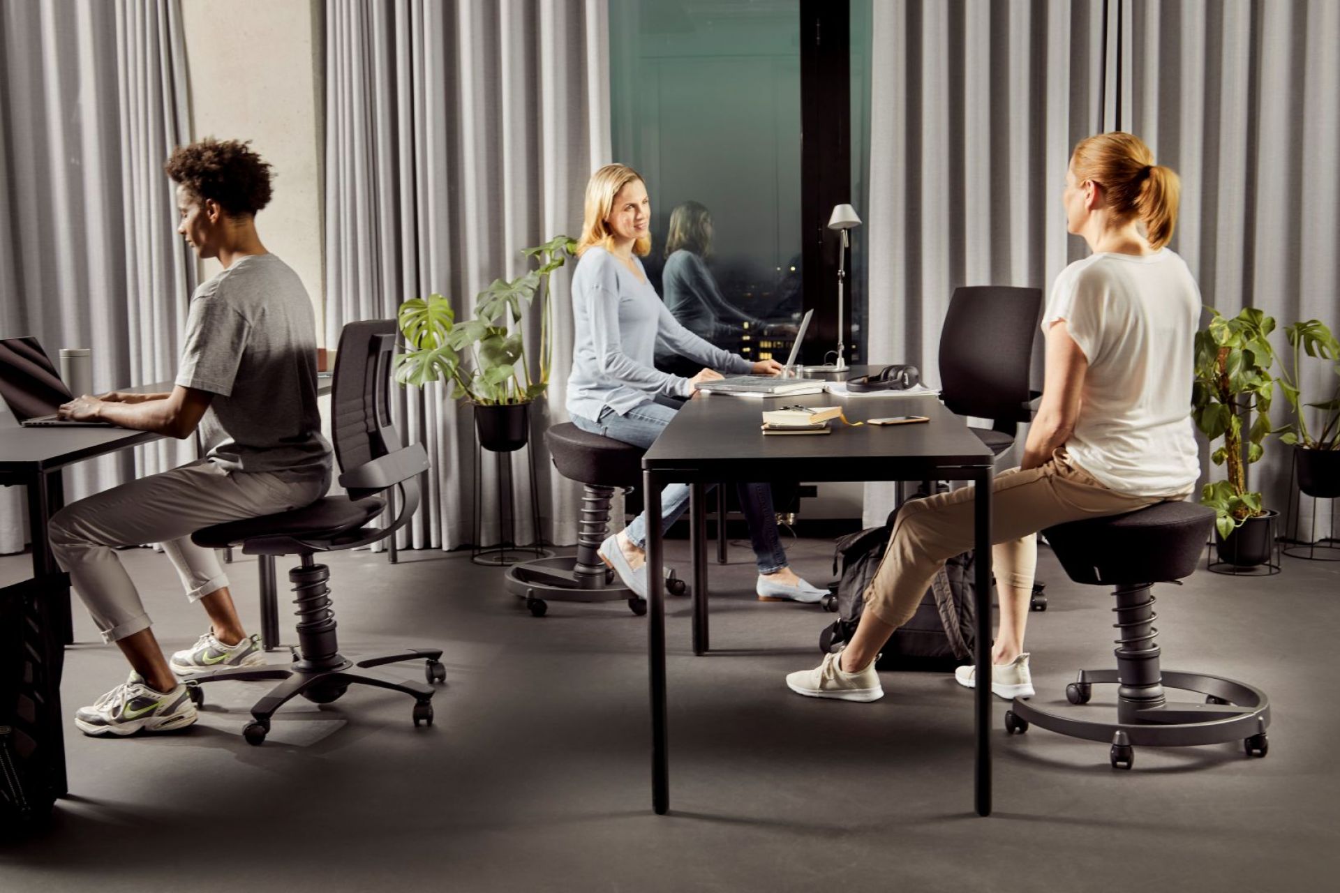 Büro mit Personen auf Swopper Hocker, aktiv sitzend an Schreibtischen. Ergonomische Büromöbel für dynamisches Sitzen.