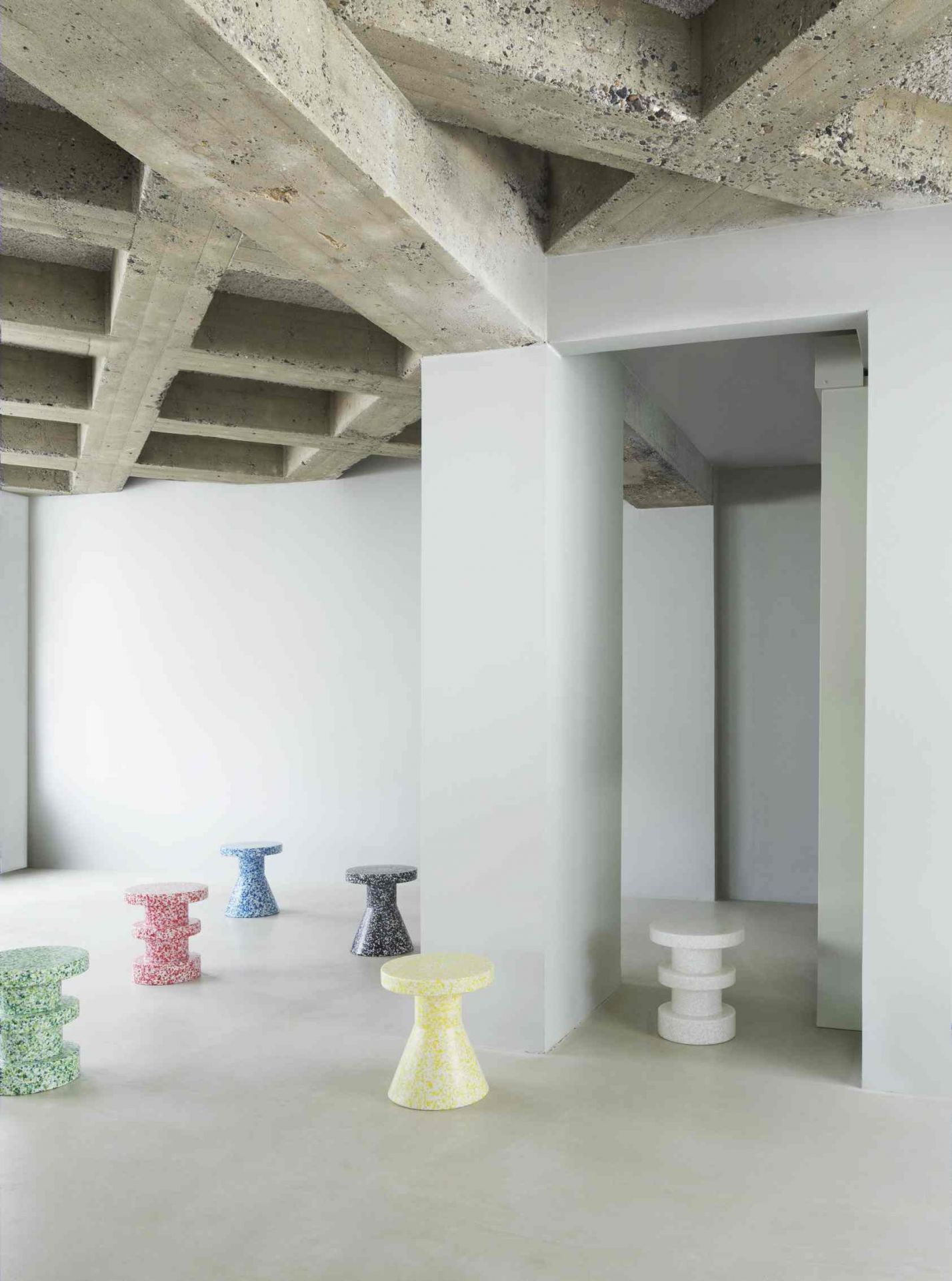 Mehrere bunte Bit Stool Cone Hocker von Normann Copenhagen in einem minimalistischen Raum mit Betonstruktur.