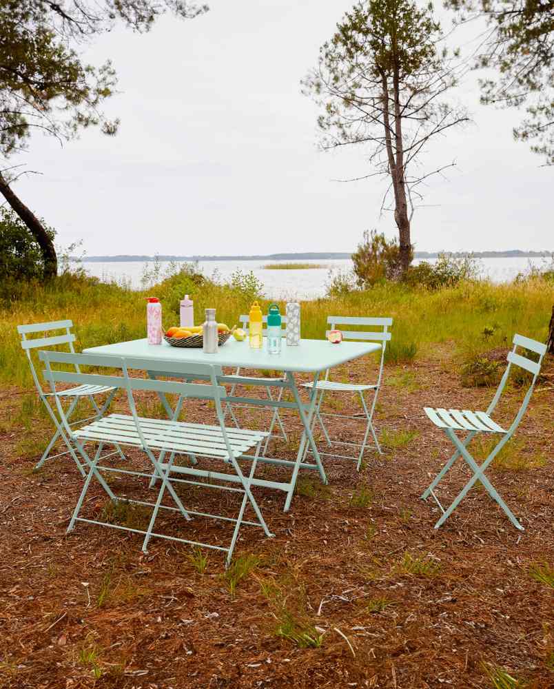 Hellblaue Fermob Bistro Gartenmöbel: Klappbank, Stühle und Tisch im Freien am See.