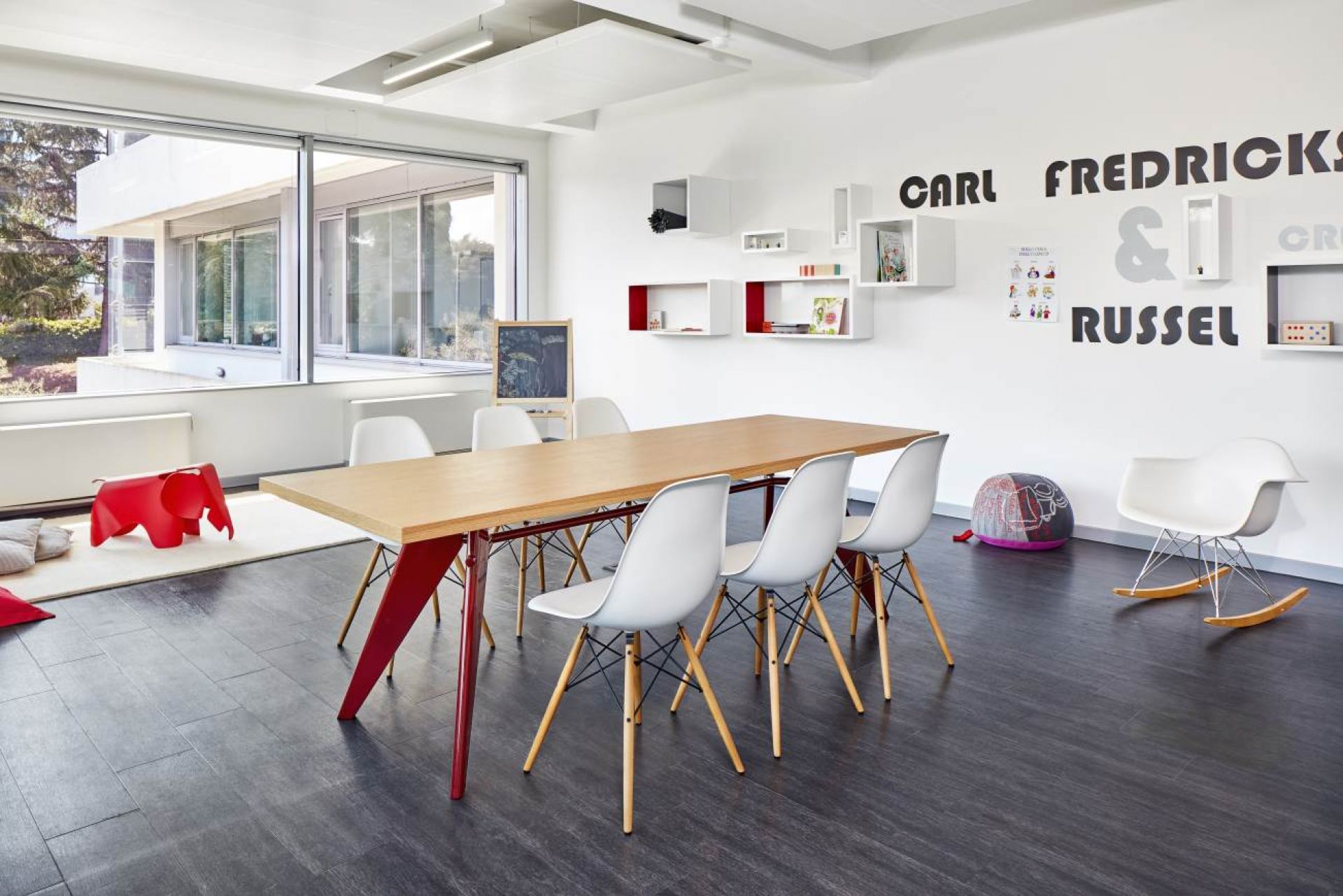 Vitra EM Table Holztisch, 240 cm lang, mit roten Beinen und weißen Stühlen.