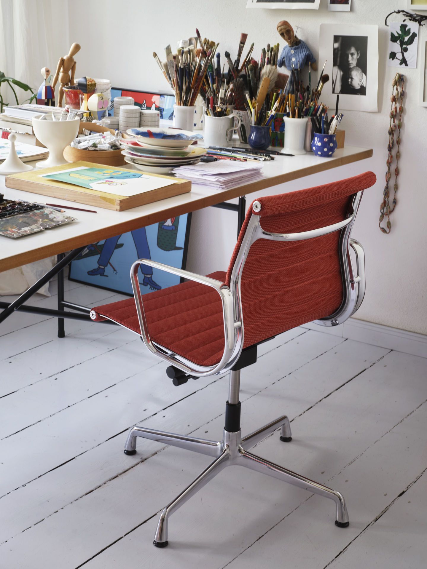 Nahaufnahme eines roten Vitra Aluminium Chair EA 131 Bürostuhls mit Chromgestell vor einem Schreibtisch.
