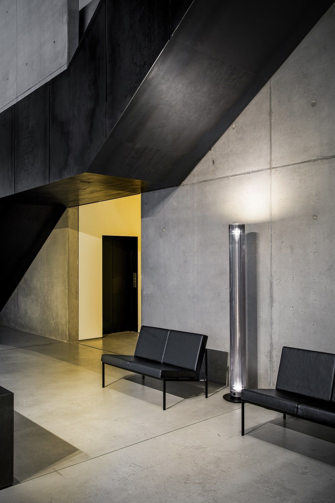 Twilight Stehleuchte SCHWARZ EDITION von Belux in modernem Ambiente mit Betonwand und schwarzen Sitzbänken.