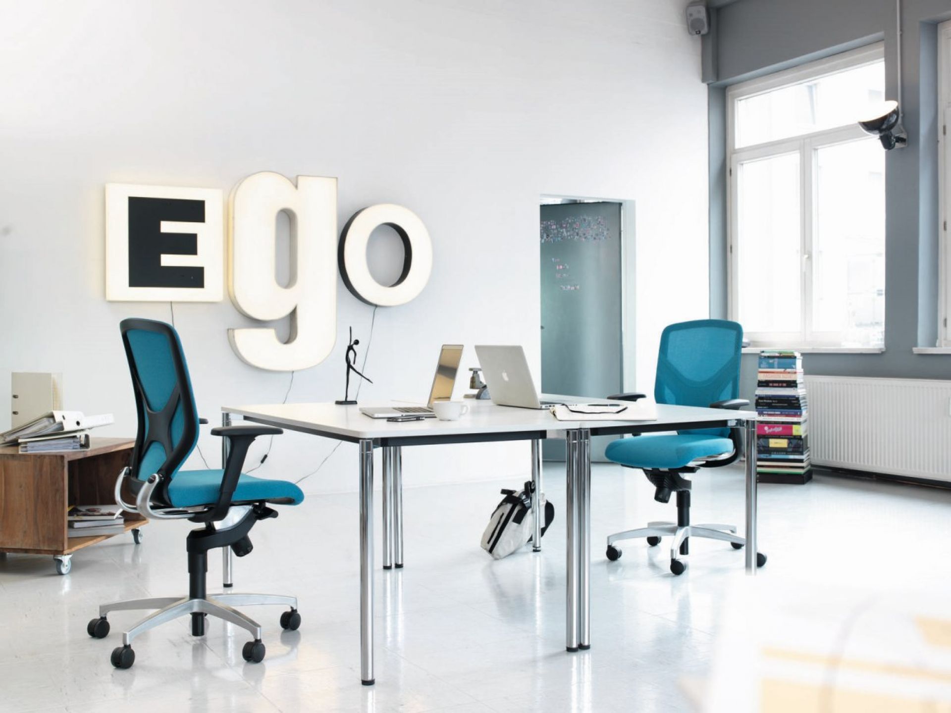 Büro mit zwei blauen Bürostühlen, weißem Schreibtisch, Laptops und Dekoration für modernes Arbeitsambiente.
