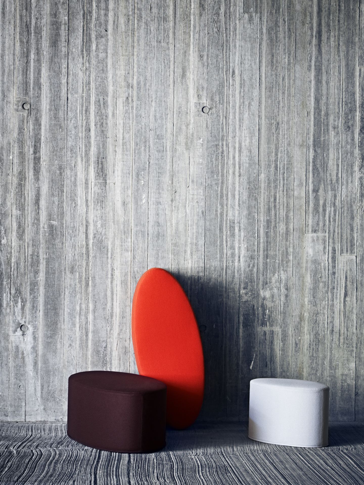 Bon Bon Hocker in Braun, Weiß und Rot vor einer Betonwand, moderne Sitzmöbel für Wohnzimmer.