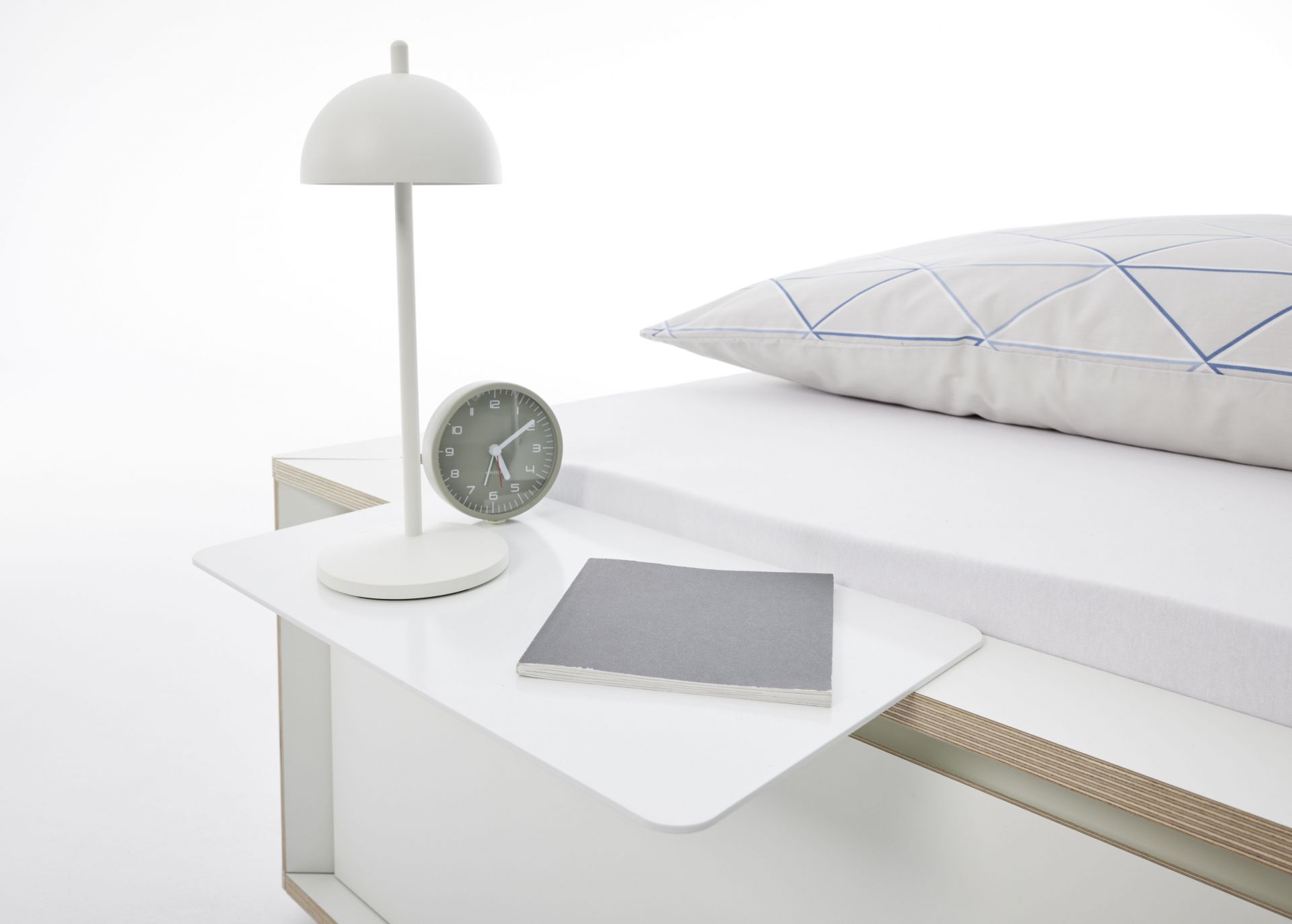 Spaze Bett von Müller Möbelwerkstätten mit Nachttisch, Lampe, Buch und Uhr in minimalistischem Design.