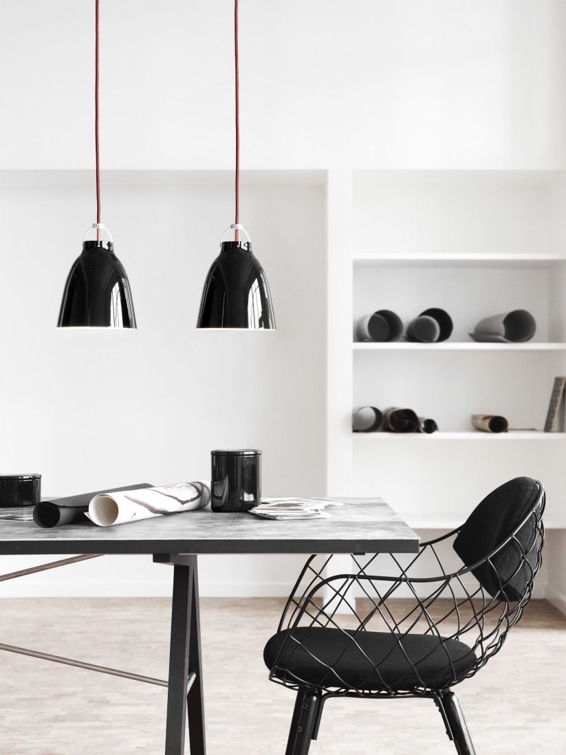 Zwei schwarze Caravaggio Pendelleuchten von Fritz Hansen hängen über einem Esstisch in einem minimalistischen Raum.