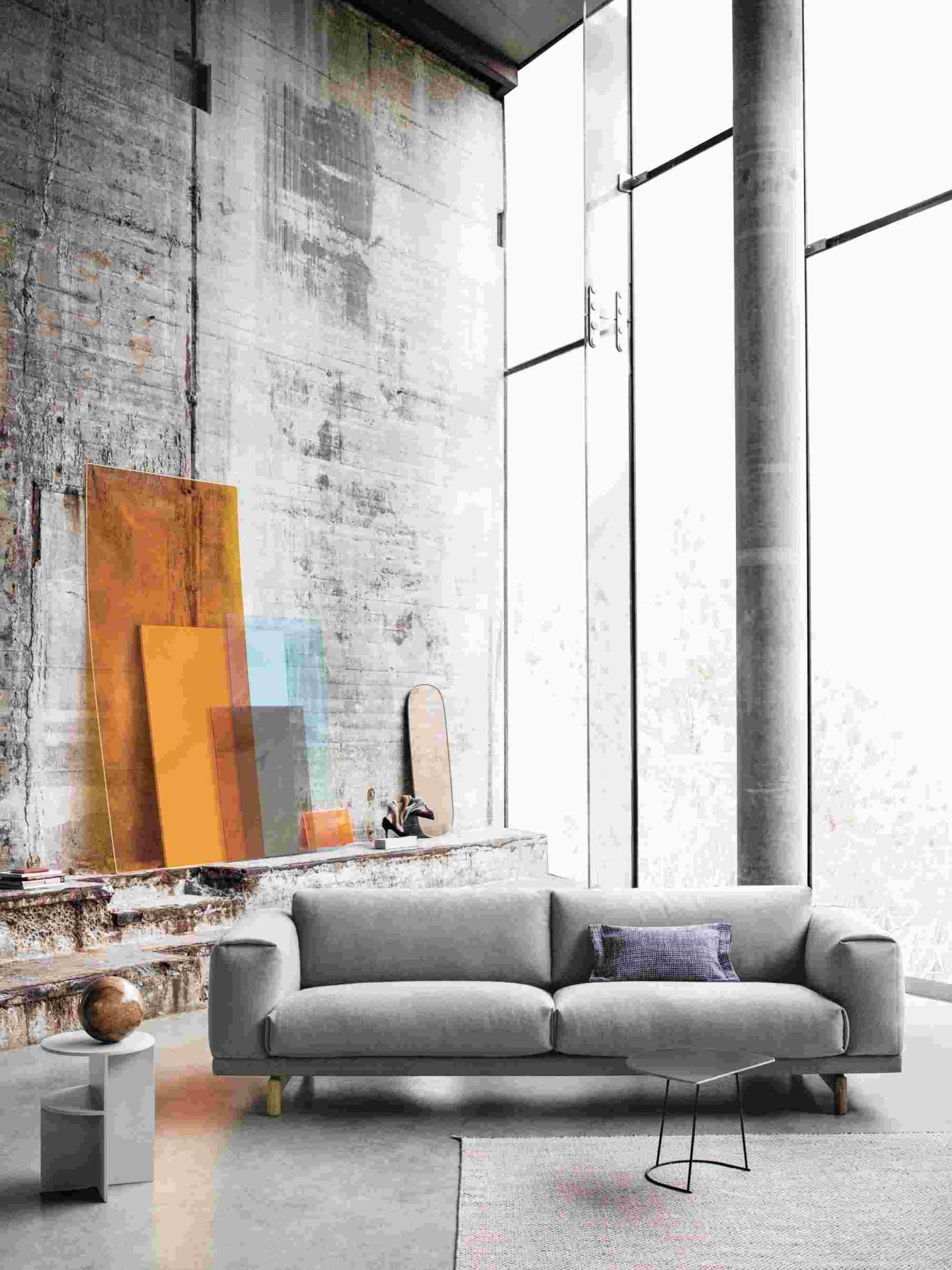 Graues Muuto Rest Sofa 2-Sitzer vor Betonwand mit Dekoration und großem Fenster, modernes Wohnzimmer Design.