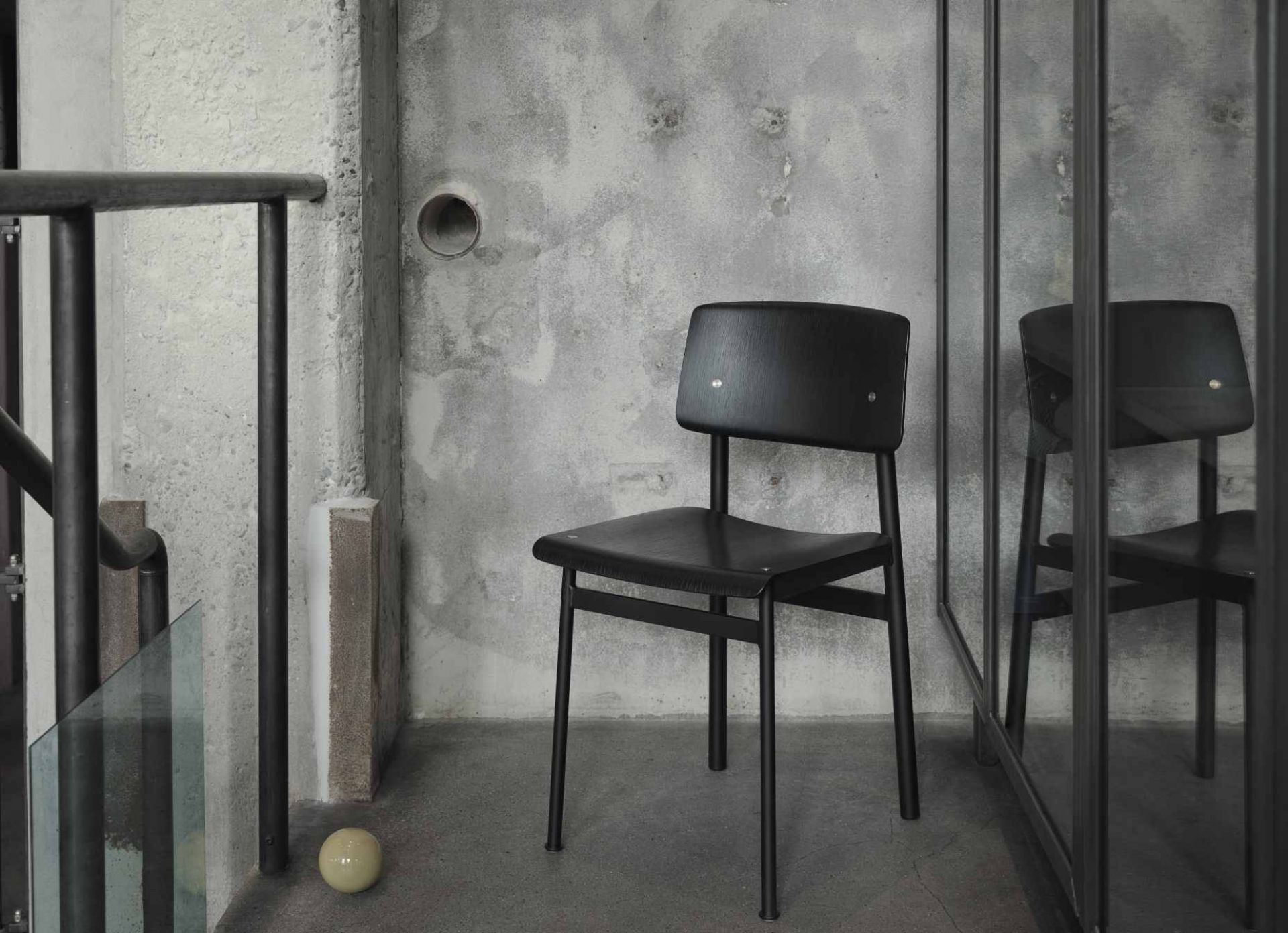 Schwarzer Loft Chair Stuhl von Muuto vor einer Betonwand, minimalistisches Design, skandinavische Möbel.