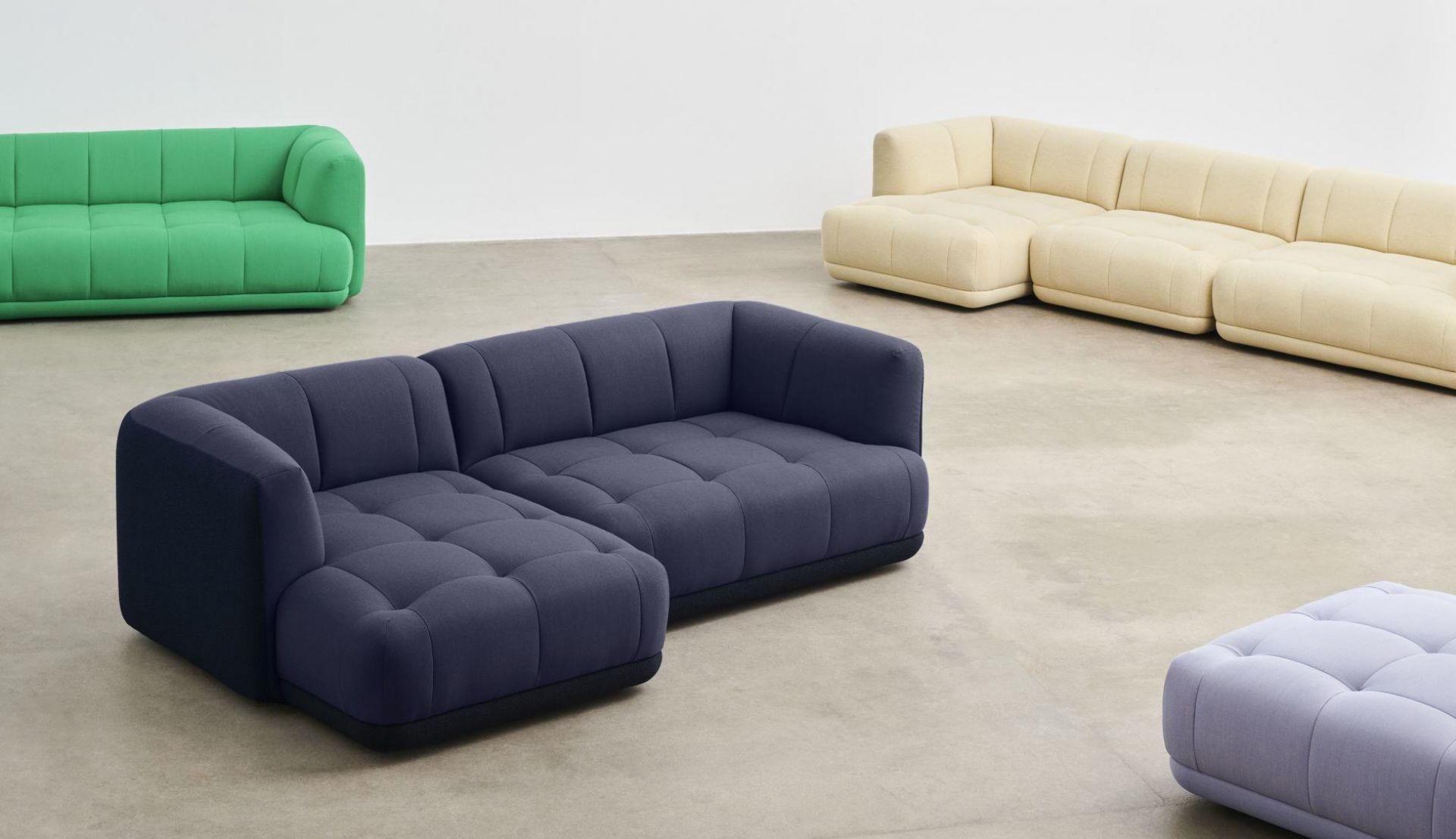 Blaues Quilton Sofa von Hay mit Ottomane und weiteren Sofas in Grün und Beige.