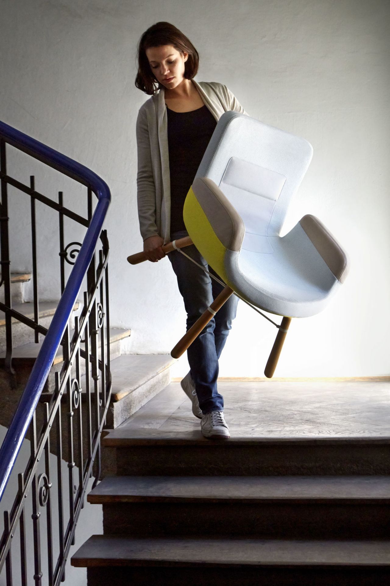 Frau trägt East River Chair Sessel von Vitra die Treppe hinunter, hellblau mit gelben Akzenten.