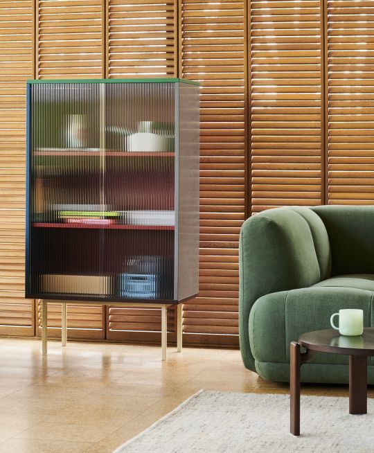 Hay Vitrine mit geriffelten Glastüren, farbigen Regalböden und goldenen Beinen im modernen Wohnzimmer.