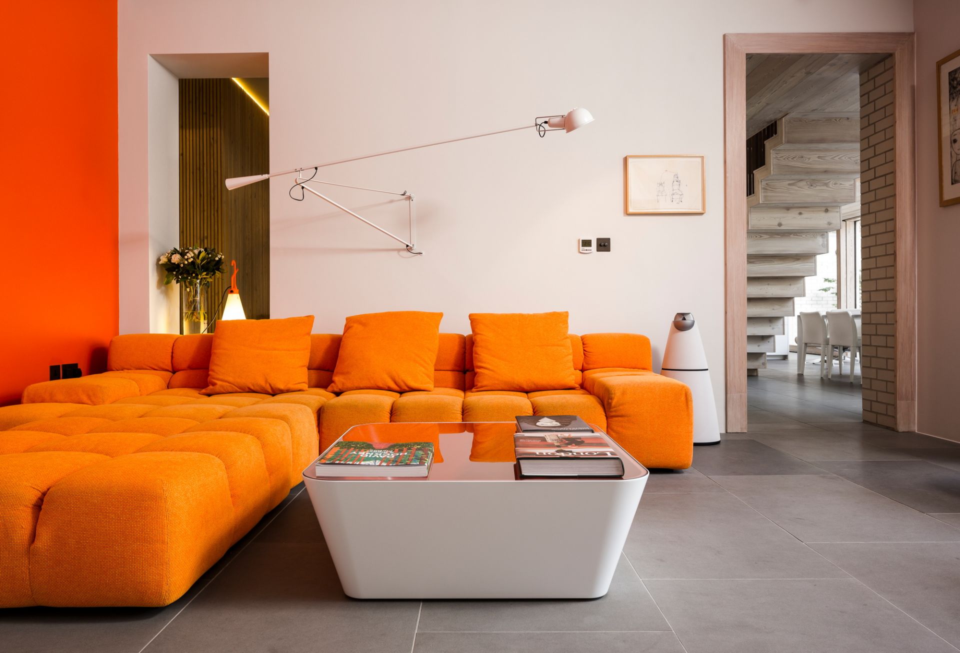Wohnzimmer mit orangefarbenem Sofa und weißer Flos Wandleuchte, verstellbare Lampe für Innenbeleuchtung.