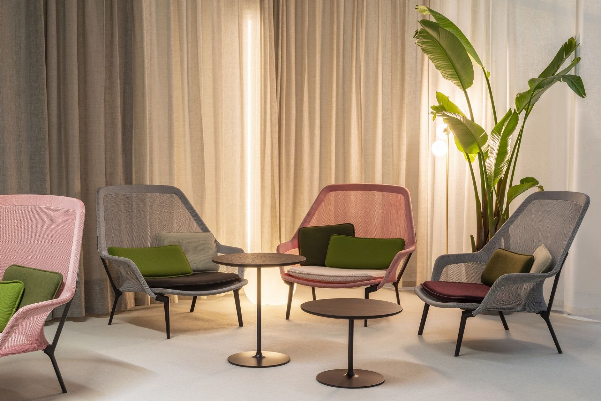 Vitra Slow Chair Sessel in Rosa und Grau mit Beistelltischen und Zimmerpflanze vor Vorhang.