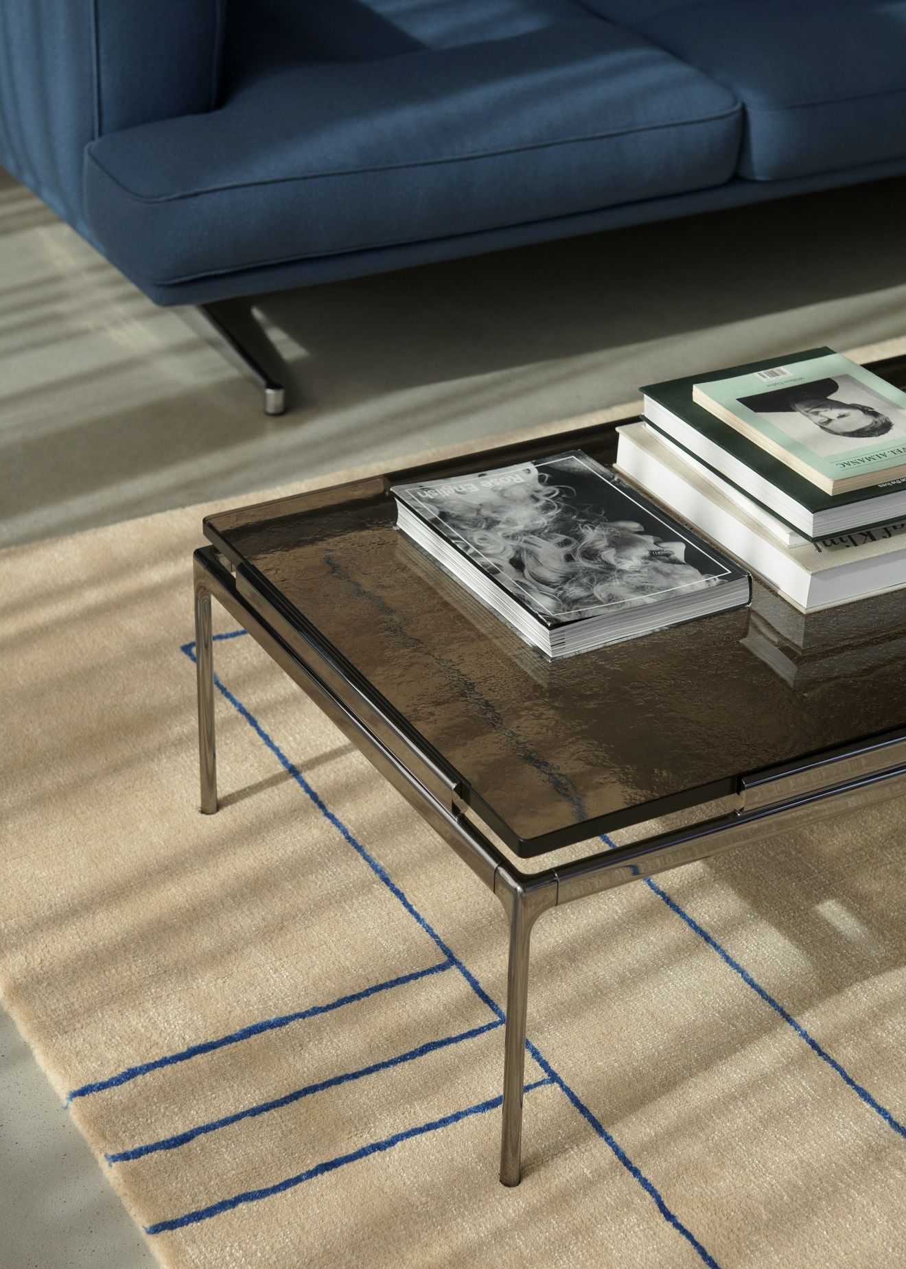 AndTradition Cruise Teppich AP11 mit blauem Linienmuster unter einem Couchtisch in Wohnzimmer-Szene.