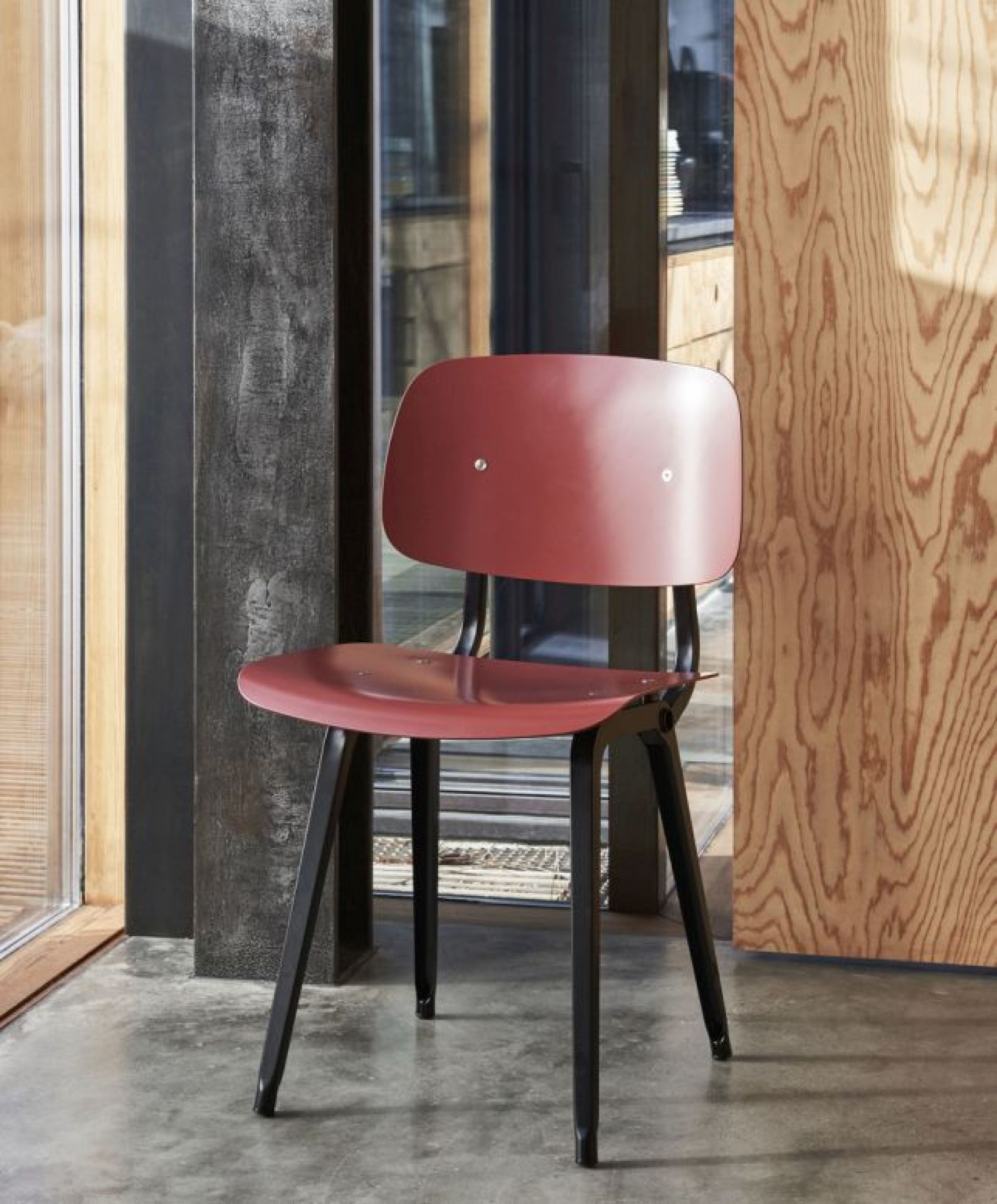 Roter Revolt Chair Stuhl von Hay mit schwarzem Gestell vor modernem Hintergrund.