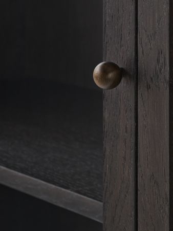 Detailaufnahme der AndTradition Trace SC87 Vitrine: Dunkles Holz, runde Türklinke und Regalböden im Innenraum.
