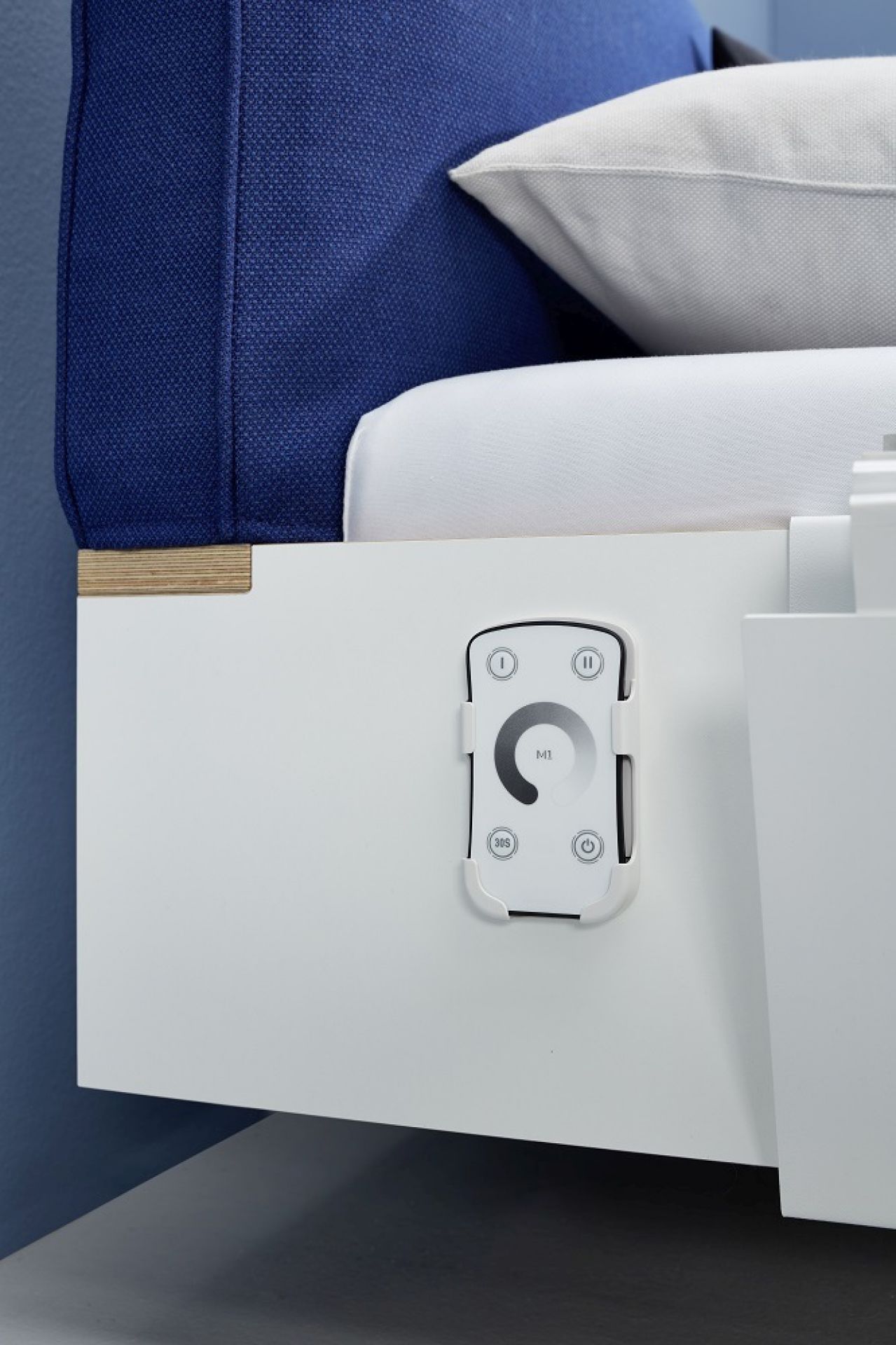 Flai Einzelbett von Müller Möbelwerkstätten mit blauen Kopfteil und Fernbedienung für Beleuchtung.