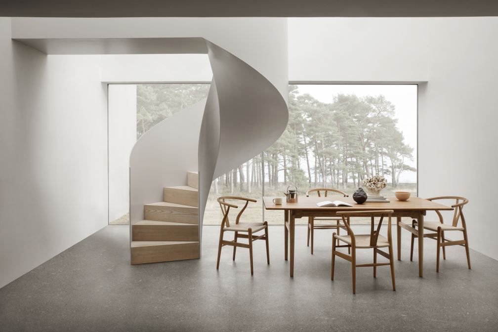Esszimmer mit Teak-Esstisch und sechs CH24 Wishbone Stühlen von Carl Hansen & Søn vor Fenster und Wendeltreppe.