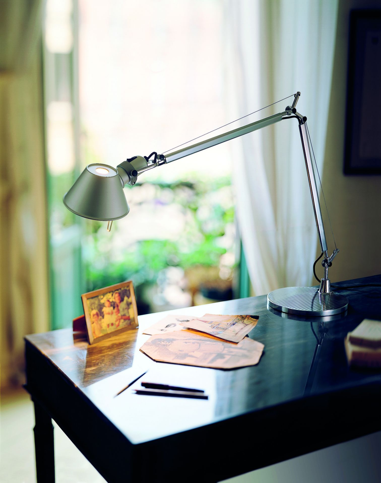Silberne Artemide Tolomeo Tischleuchte auf dunklem Schreibtisch mit Fotos und Stiften, indirektes Licht.